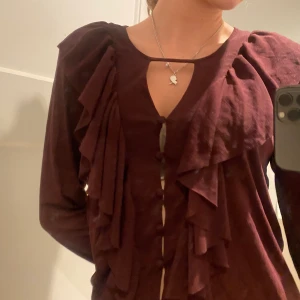 Topp med volanger  - Vinröd långärmad topp med knappar i mitten och volanger runt omkring. Superskönt material!❤️🍇💓