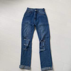 mörkblå jeans med hål på knäna. jeansen har medelhög midja. använda få gånger. storlek xs-xxs. köparen står för frakten. 