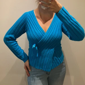 Tjockstickad tröja turkos.  - Tjock, varm och mysig omlottröja med söt knytdetalj i sidan. Ytludd kan förekomma; tas bort med noppmaskin.  Hel och ren. Inga anmärkningar.  Djur- & rökfritt hem.  Rensar ur min walk-in-closet, så kolla in å fynda! Samfraktar! 