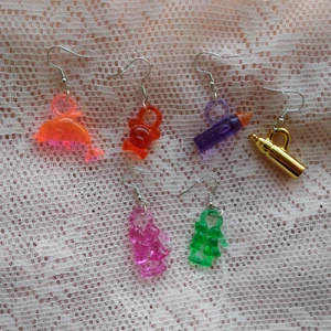 Udda örhängen - Mixa och matcha med dessa söta örhängen! Jag har gjort dem av plasthängen från en loppis. Det är en rosa delfin, en röd nalle, en guldig och en lila nappflaska samt ett rosa och ett grönt kärlekspar (det rosa är lite större än det gröna!) 💖 20 kr för ett par, 25 kr för alla! OBS! Jag kan inte garantera att hängena är nickelfria, så undvik dessa om du är allergisk! 