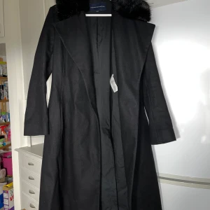 French connection kappa  - Lång kappa från french connection. Fint skick. Upphängningsgrejen i nacken trasig (kan skicka bild), i övrigt super fint skick.  Material: 75% Virgin wool, 20% polyamidenylon, 5% cashmere. Pälskrage: 67% akryl, 17% modacryl, 16% polyester, 35% bomull.    