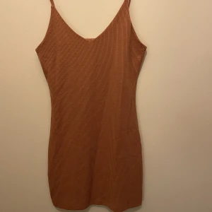 Ribbad klänning  - Figurnära kort klänning i ribbat material med tunna axelband. Färgen är rosa/brun/beige
