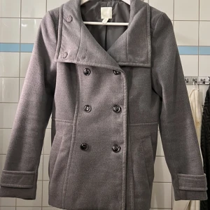 Hm kappa  - Grå HM kappa som har använt en gång, väldigt fin kvalitet då jag har bara använts en gång. Det enda är att tråden på knaparna har repas up,anarsh väldigt fin. Köpte den för 399kr då den är knappt använd så säljer jag den för samma pris.  Skriv om frågor 