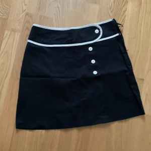 Kjol  - Kort svart kjol med vita detaljer.