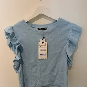 Zara T-shirt med volanger storlek M - Helt oanvänd och original lappen sitter kvar. Fin ljusblå färg, lite kortare modell och normal i storleken. 45kr+frakt