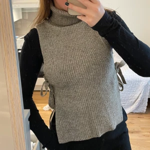 Stickad väst med hög krage  - Fin väst man knyter i sidan från Indiska. Använd 1 gång. Mycket stretch. Välstickat och bra material. Mer beige/bruna inslag i verkligheten än vad som kommer fram på bild.