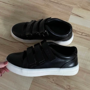 NAKD skor - Skor från NA-KD med svart skinnimmitation och kardborreband som spänne! Lånade bilder, skriv för fler bilder. Använda men inget synligt slitage alls utan i väldigt fin skick fortfarande! Köparen står för frakten ☺️