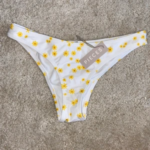 Bikiniunderdel Pieces S - Ett par vita bikinitrosor med gula blommor på. Superfina och bra material. Storlek S men känns ganska små i storleken. Självklart aldrig använda, med lappen kvar!🤍 