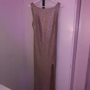 Lång, guldglittrande balklänning med öppen rygg. Klänningen köptes år 2019 och kan därför inte köpas i butik längre, klänningen användes dock bara en gång är därför i nyskick! Otroligt fin att ha på en bal eller liknande tillställningar :) (Nypris: 999 kr)
