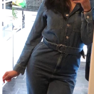 Jumpsuit i denim med knyt i midja  - Jumpsuit i denim med knytskärp i midjan, från NA-KD.  Endast använd 1 gång så är i nyskick. Nypris: 599 kr.  Storlek: 36 