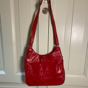 Röd axelväska/handväska  - Röd axelväska. Kan hängas på en axel men även korshängas över axlarna. Relativt rymlig. Rymmer lätt: mobil, plånbok, nycklar etc + en mindre bok/block.