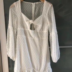 Studentklänning - Säljer min fantastiska studentklänning. Endast använd en gång och är som ny. Den går att knyta fram och har dragkedja bak. Den går till mitten av låren har har långa armar och små fina prickar på sig.