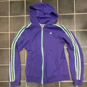 Adidaskofta - Lila Adidaskofta med fler färgade streck. Stor o bra luva med fungerande dragkedjor.