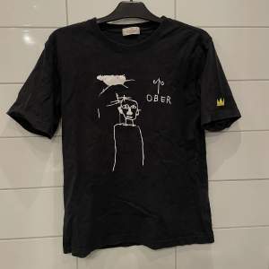 T-shirt från/av Jean-Michel Basquiat. ”Abstrakt” motiv och den klassiska kronan på ena tröjarmen.