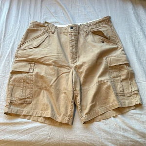 Polo ralph lauren shorts - Beiga polo ralph lauren shorts som köptes för ett tag sen på secondhand, har inte använt sen de köptes. Midjan är 115cm men kan justeras till 100cm Priset kan diskuteras :) Bara i Göteborg