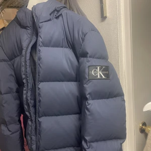 CALVIN KLEIN DUNJACKA HERR LARGE -  Använd men i nyskick inga hål eller fläckar. Nyss kemtvättad  Tröttnat på den och vill ha en annan modell & märke.  Säljes för 1000kr p.k.d. vid snabb affär.  Stl  Large.  Kan även tänka mig att byta mot annat märke och dunjacka. Peak med luva mm        