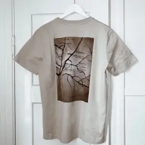 Beige oversized T-shirt från UF-företag. Tryck på ryggen och på framsidan står det ”be better for the world”. Tillverkad i återvunnen ekologisk bomull.  Trycker på baksidan är framtaget av en konstnär och t-shirten finns i storlek xs-xl. Unisex