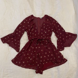 Playsuit - Kort byxdress i vinröd färg med mönster av guldiga vindruvor! Superfin till sommarfest eller festival! Storlek S men känns mer som XS. 