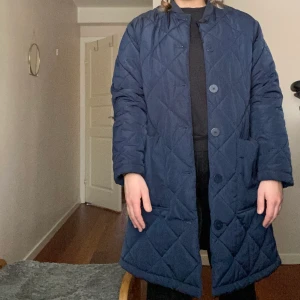 Lång quiltad kappa  - Lång quiltad kappa från Lindex. Köpt förra året. Perfekt till vår och höst! Tunt vadderat. Använd ett fåtal gånger. Storlek S.