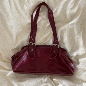 Rizzo väska - Vinröd väska från Rizzo. Längd ca 35 cm, höjd ca 18 cm. Har tre stora fack och två små dragkedjefack. 