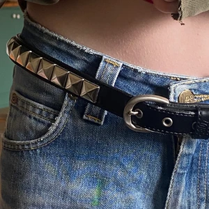 Lowlife skärp - Lowlife skärp med nitar. Köptes på 2000 talet av en släkting till mig men är fortfarande i bra skick. Hela skärpet är 110cm, från knäppet till det yttersta hålet är det 105cm och till det innersta hålet är det 90cm. Sen finns det också utrymme att göra egna hål. Hon på bilden har xs och det är för stort på henne