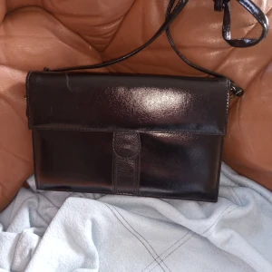 Svart kuvert väska med rem. - Helt ny och oanvänd kuvertväska svart med rem och i skinnimitation liknande material .hämtas i Skene alt skickas o köpare betalar frakten o Swishbetalning tillämpas alt kontant betalning .