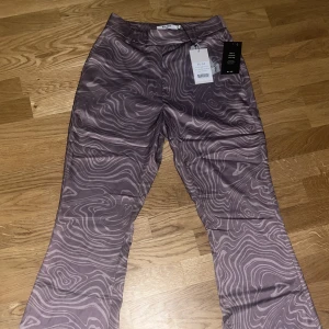 Kostymbyxor i satin - Lila mönstrade kostymbyxor i satin. Nyskick, lapp finns kvar! Från NA-KD. Storlek 34. Säljer pga för små. Köparen står för frakt💓Pris kan diskuteras!