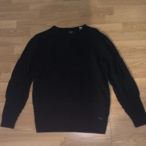 Gant svart stickad tröja  - Svart stickad tröja från Gant, med en liten ligga längst ner på tröjan 