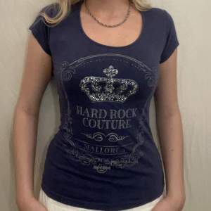 Blå T-shirt med silvrigt och glittrigt tryck av Hard Rock Café. Fint skick. Sitter så här på någon som brukar ha XS/S. 