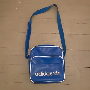Axelremsväska adidas - Jag säljer nu en blå adidas axelmremsväska eftersom jag inte använder den längre, bra kvalitet. Man kan knappt se att den är använd om man inte kollar nära! Skriv privat för fler bilder eller andra frågor! Pris kan absolut diskuteras! Bredd 29cm, längd 30