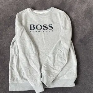 grå Hugo boss tröja med en röd detalj på bröstet(design) och det är inget smuts eller hål på tröjan. Mycket fint skick och är använd få gånger då jag växte ur den snabbt! Storlek 16-M men jag skulle säga att den är xs-s i herr och Medium i barn ! 