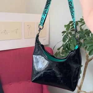 Väska adidas - En mellanstor axelremsväska från adidas, svart och grön, med justerbart och avtagbart band. Ursprungspris 500kr. Knappt använd!