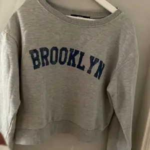 En grå croppad sweatshirt med blå text på. Skulle även passa som en small. Skriv för fler bilder 