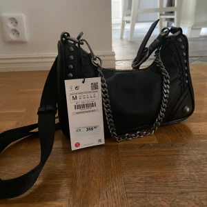 Zara Väska  - Svart Zara väska med långt sjysterbart axelband. Går att ha krossat över axeln eller hängandes på axeln. Avtagbar kedja, liten men rymlig. Prislapp kvar. 