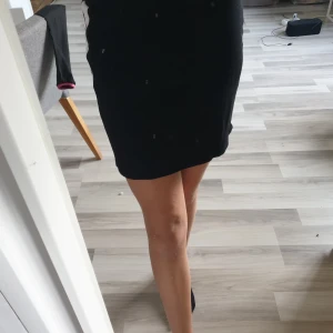 Svart kjol - En svart kjol med vit rand på vardera sita med silverknappar på. Kjolen är ifrån Lindex och är som ny. Säljer pga att den inte kommit till användning eftersom det inte riktigt är min stil längre