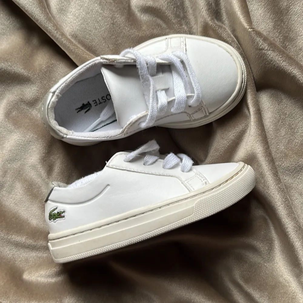 Söta Lacoste sneakers för barn storlek 21 i vitt och silver. Använt några gånger. Köpta i Usa i butiken på Soho i NY. . Skor.