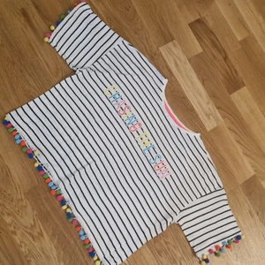 Tröja  - En vit tröja med svarta ränder och hängande små bollar  Storlek: 146/152cm 