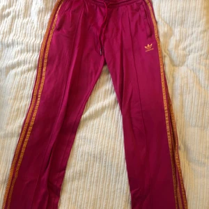 Retro rosa adidas byxor - Vintage rosa/orangea adidas byxor från 90-talet strlk M fungerar för XS-M. Byxorna är vida och sitter bra på kroppen, går att ha highwaisted eller lowwaisted.  De e väl använda men i gott skick har en fläck nere på ena benet, fråga för bild. 
