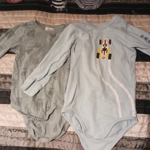 2 bodies barn - Från vänster: 1 st grön bodies med ugglor märket newbie storlek 80. 1 st ljusblå med racerbilmotiv från ellos storlek 80. Sparsamt använda.