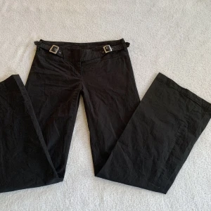 Svarta kostymbyxor - Lågmidjade utsvängda kostymbyxor med spännen i midjan, från märket Patrizia Pepe! Står stl 40 men passar mig som brukar ha XS/S och är 173 cm, midjemåttet är 74 cm och innerbenslängden 82 cm! 💘