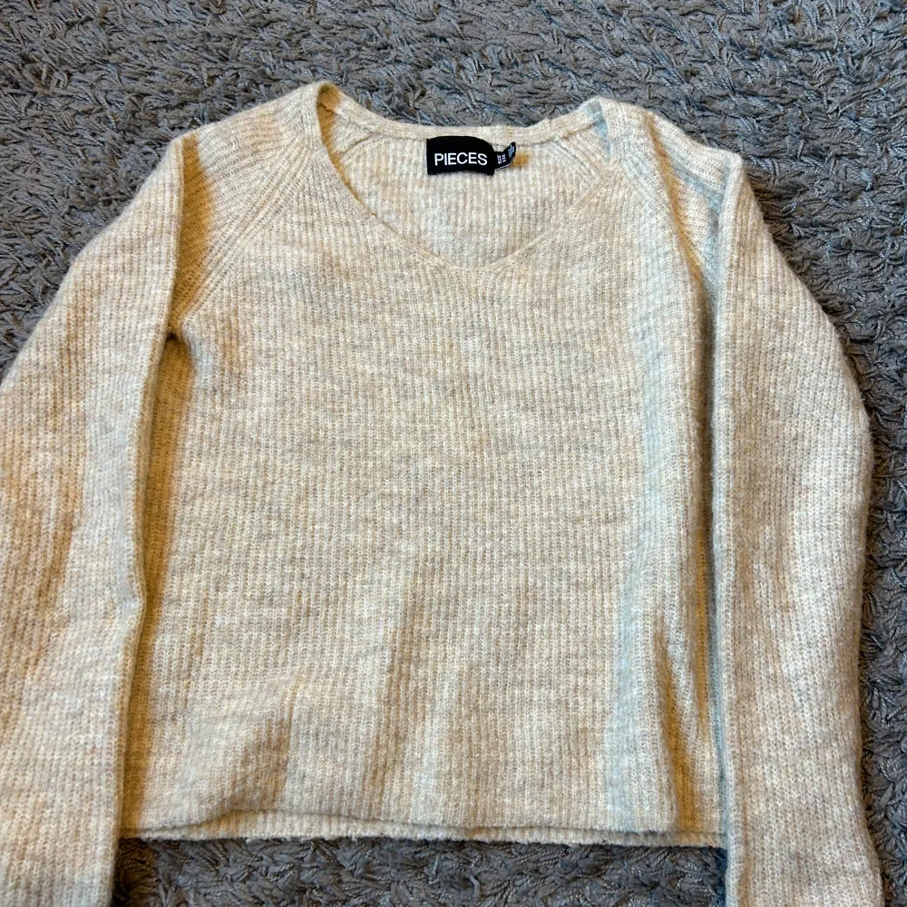 Mysig beige stickad tröja från Pieces i storlek XS. Perfekt för höst och vinter med sin varma och bekväma design. Tröjan har en v-ringad hals och långa ärmar. Passar perfekt till både jeans och kjol! Knappast använd. Tröjor & Koftor.