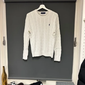 Vit stickad tröja från Polo Ralph Lauren - Säljer en klassisk vit stickad tröja från Polo Ralph Lauren. Den har ett snyggt kabelstickat mönster och den ikoniska loggan broderad på bröstet. Perfekt för både höst och vinter, med långa ärmar och en bekväm passform. Passar till alla tillfällen! Storlek M. Bra skick. Märkeströja. 