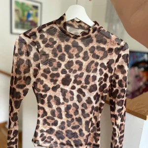 Leopardmönstrad meshtröja - Säljer en supercool leopardmönstrad meshtröja med lång ärm. Perfekt för en utekväll eller när du vill sticka ut lite extra. Tröjan är tight och har en hög hals, vilket ger en snygg och stilren look. Materialet är lätt och luftigt, vilket gör den bekväm att bära.