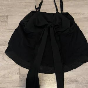 Svart linne med rosett fram - Ett svart linne med en rosett fram, sjusterbar band.