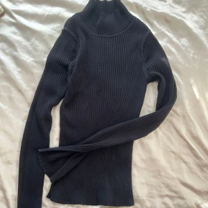 Svart ribbad polotröja från KappAhl - Säljer en stilren svart ribbad polotröja från KappAhl i storlek XS. Perfekt för kyliga dagar med sin höga krage och långa ärmar. Tröjan är i nyskick! 
