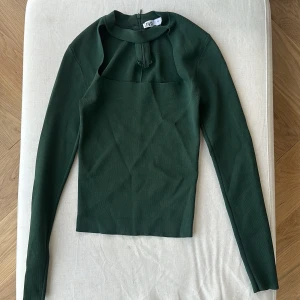 Mörkgrön långärmad topp från Zara - Säljer en stilren mörkgrön topp från Zara i storlek S. Den har en unik design med en dragkedja bak och långa ärmar. Perfekt för höst och vår, och kan enkelt kläs upp eller ner beroende på tillfälle. 