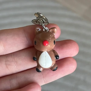 Nyckelring med renmotiv - Söt nyckelring med en liten renfigur i brunt och vitt. Den har en röd nos och svarta detaljer på tassarna. Perfekt som en julig accessoar eller present. Fäst i en metallkedja med en enkel klämma för att fästa på väskor eller nycklar.