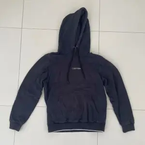 Säljer en stilren mörkblå hoodie från Calvin Klein. Den har en klassisk design med en känguruficka och justerbar huva. Perfekt för både vardag och chill. Passar bra till jeans eller joggers. Hör av dig vid intresse!