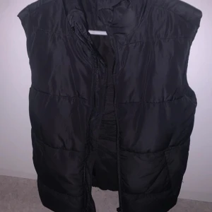 Svart dunväst från Monki - Säljer en svart dunväst från Monki i storlek dam M. Västen är perfekt för höst och vinter, med en dragkedja framtill för enkel stängning. Den är i nyskick och har en normal passform. Perfekt för att hålla värmen med stil!