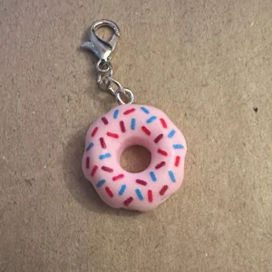 Nyckelring med rosa donut - Supergullig nyckelring formad som en rosa donut med färgglada strössel i blått och rött. Perfekt accessoar för att piffa upp dina nycklar eller väskan. Den har en praktisk karbinhake i silverfärg för enkel fastsättning. Perfekt för alla som älskar söta detaljer! 🍩